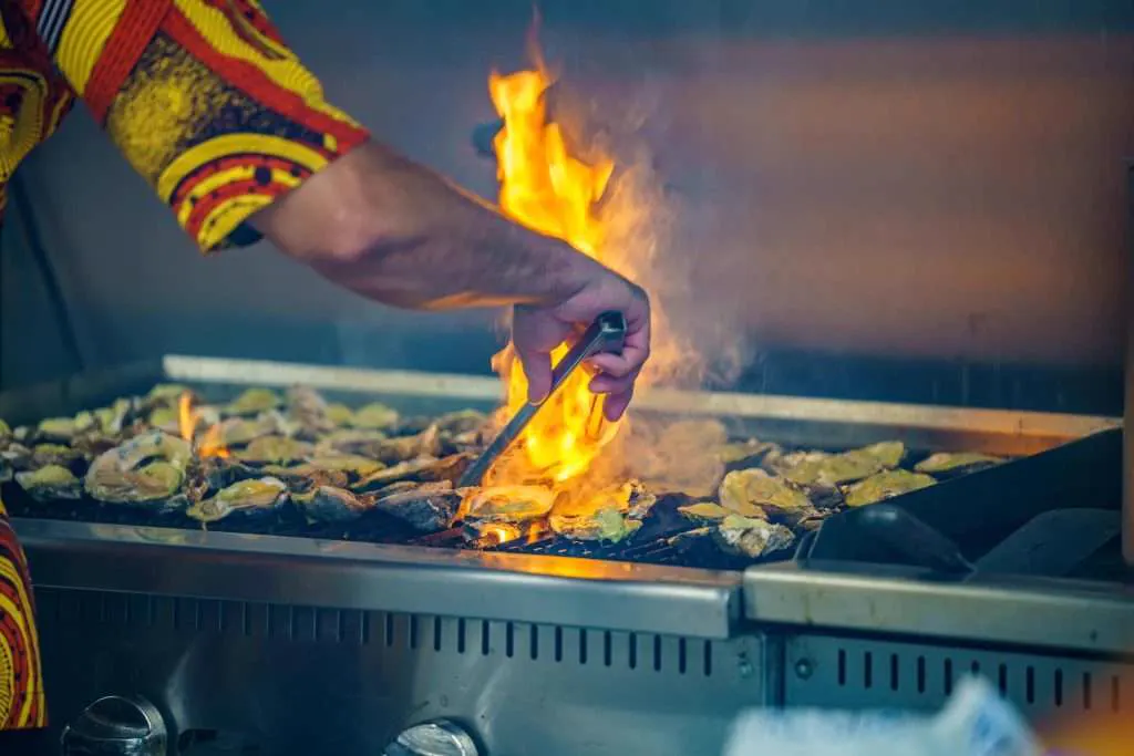 Oysters on a flaming grill, a cook's sleeve in bright African print