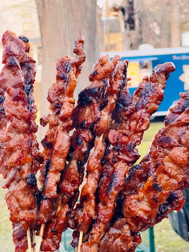 Charred beef skewers held up outdoors