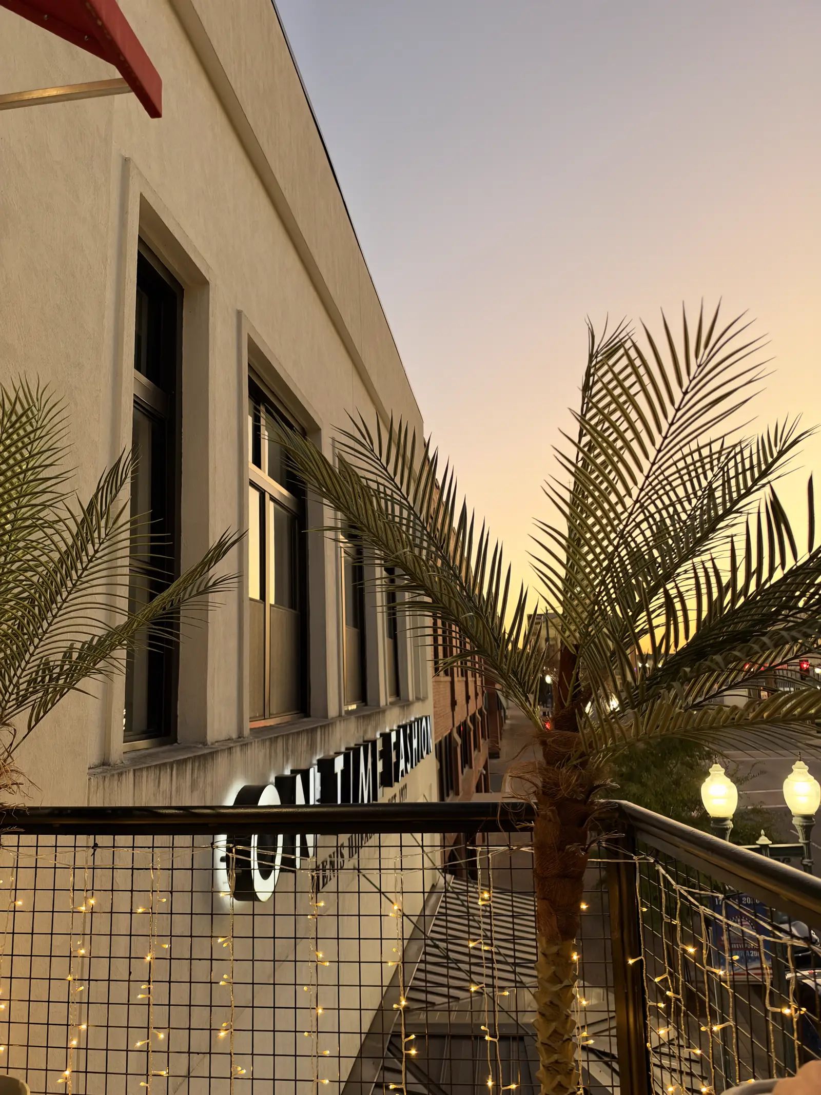 Palms and string lights along the balcony rail at sunset